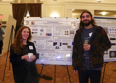 Two people posing in front of poster display