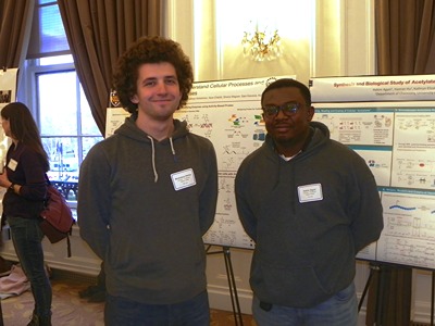 Two people posing in front of poster display
