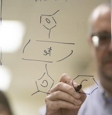 Professor draws a chemical compound on a plexiglass board